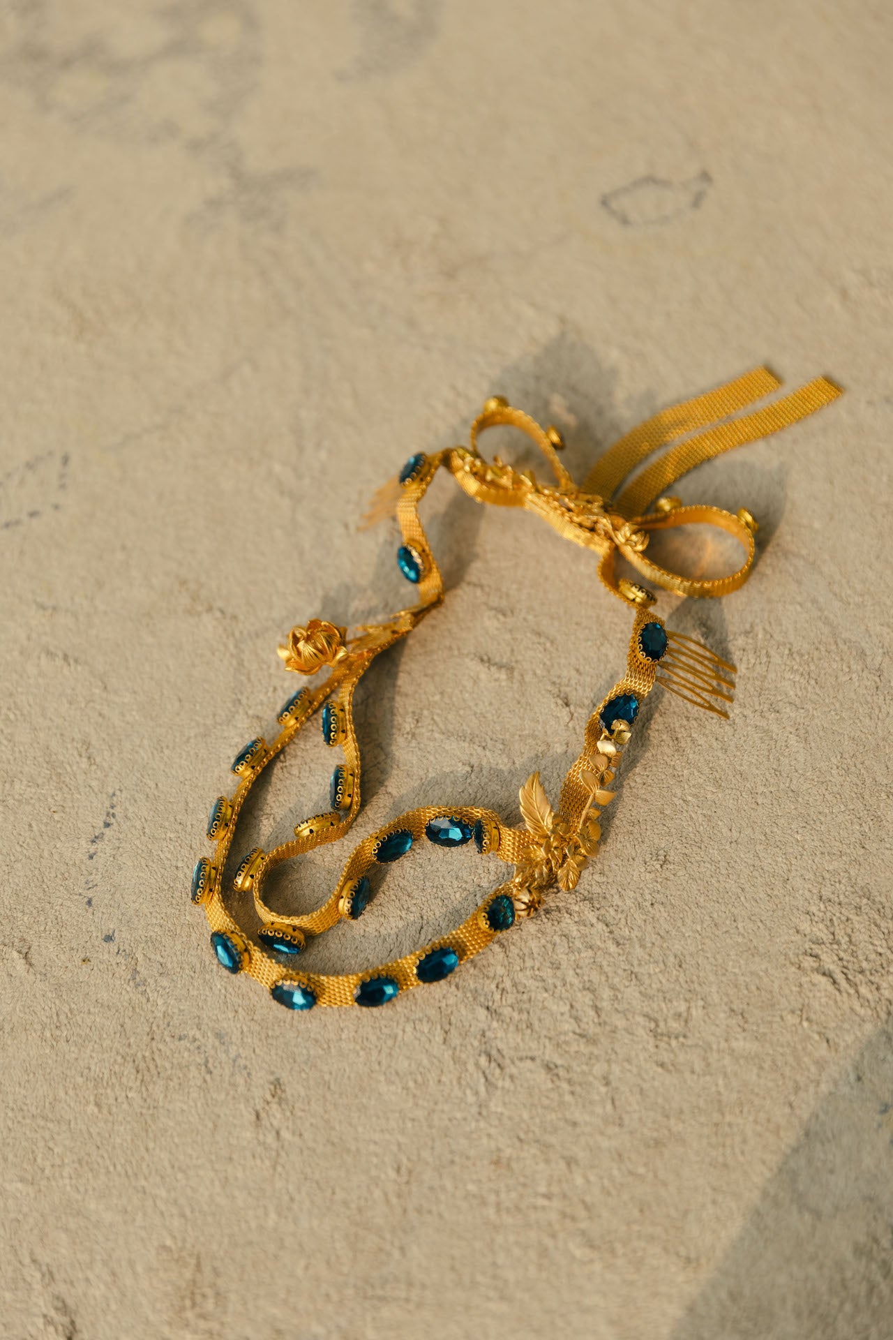 Coroa Lakkos com efeito de fita em latão com pedras azuis e flores em latão banhado a ouro fecho como um laço